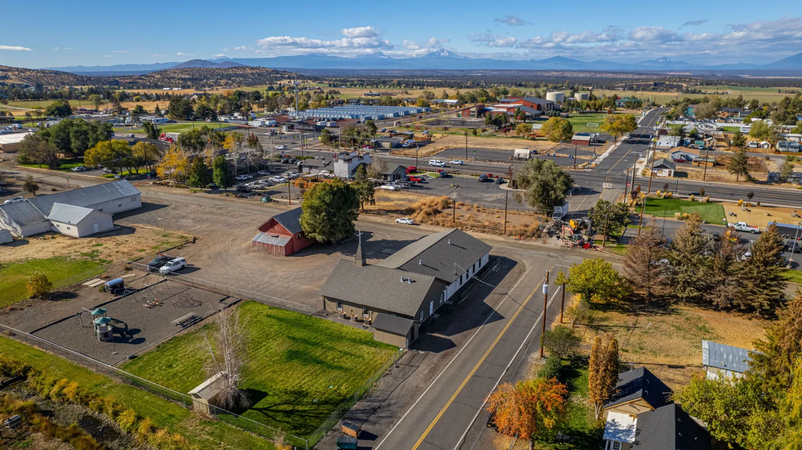 Aerial view of a Central Oregon town with rooftops, open fields and distant mountains