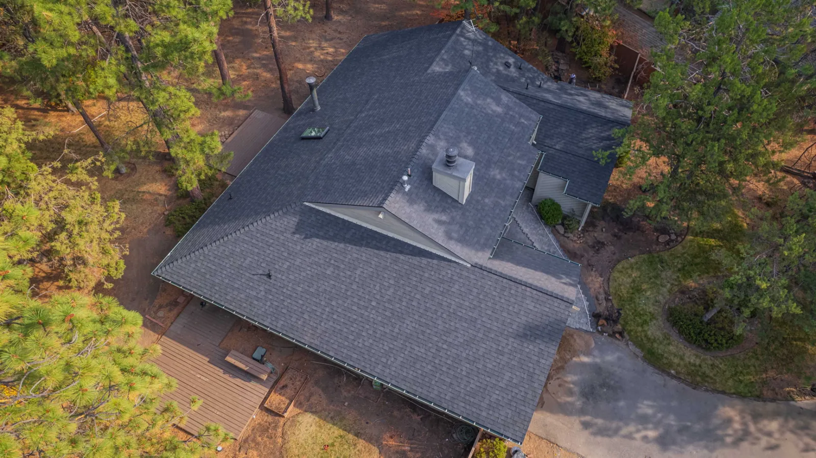 Aerial view of a completed composition shingle roof replacement on a home surrounded by ponderosa pines in Bend, Oregon