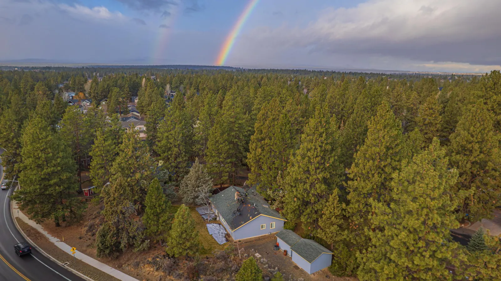 Storm clearing over a Central Oregon neighborhood with a rainbow above pine-covered rooftops