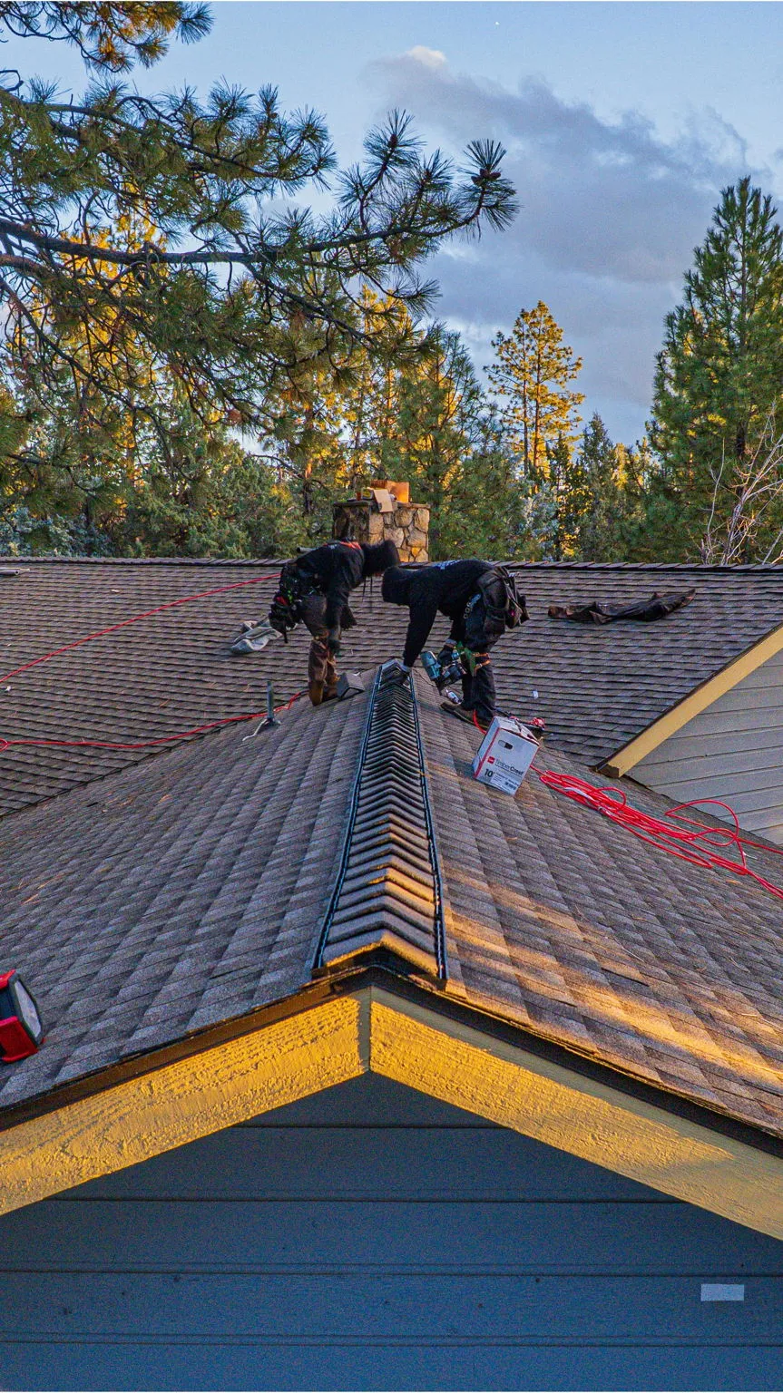 Two roofers installing ridge cap shingles at the peak